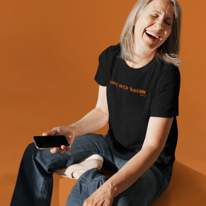 Woman sitting and laughing wearing black unisex short sleeve t-shirt 'Move Over Bacon' design on front with orange font